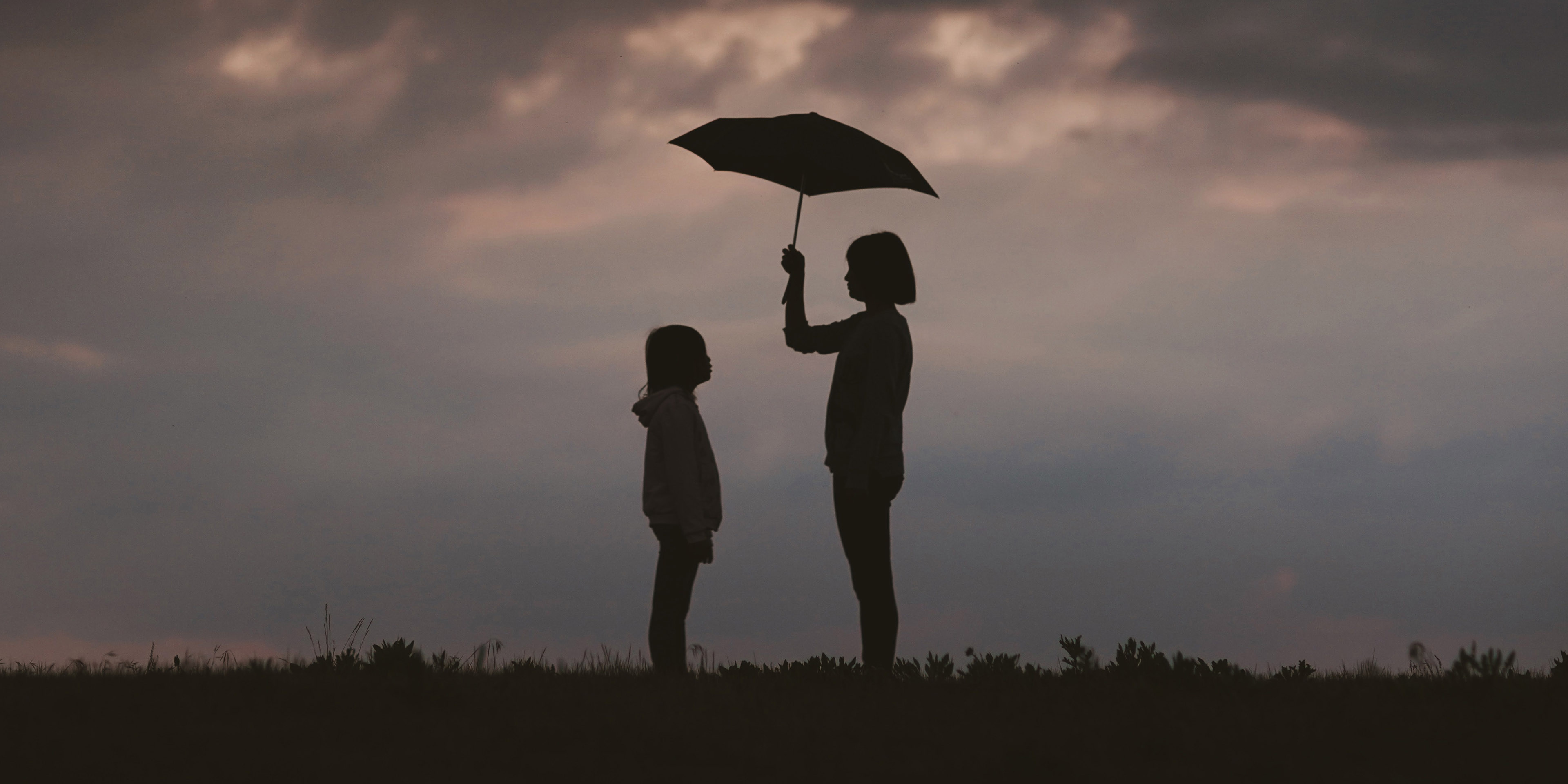 An older child holding an umbrella for a younger child.