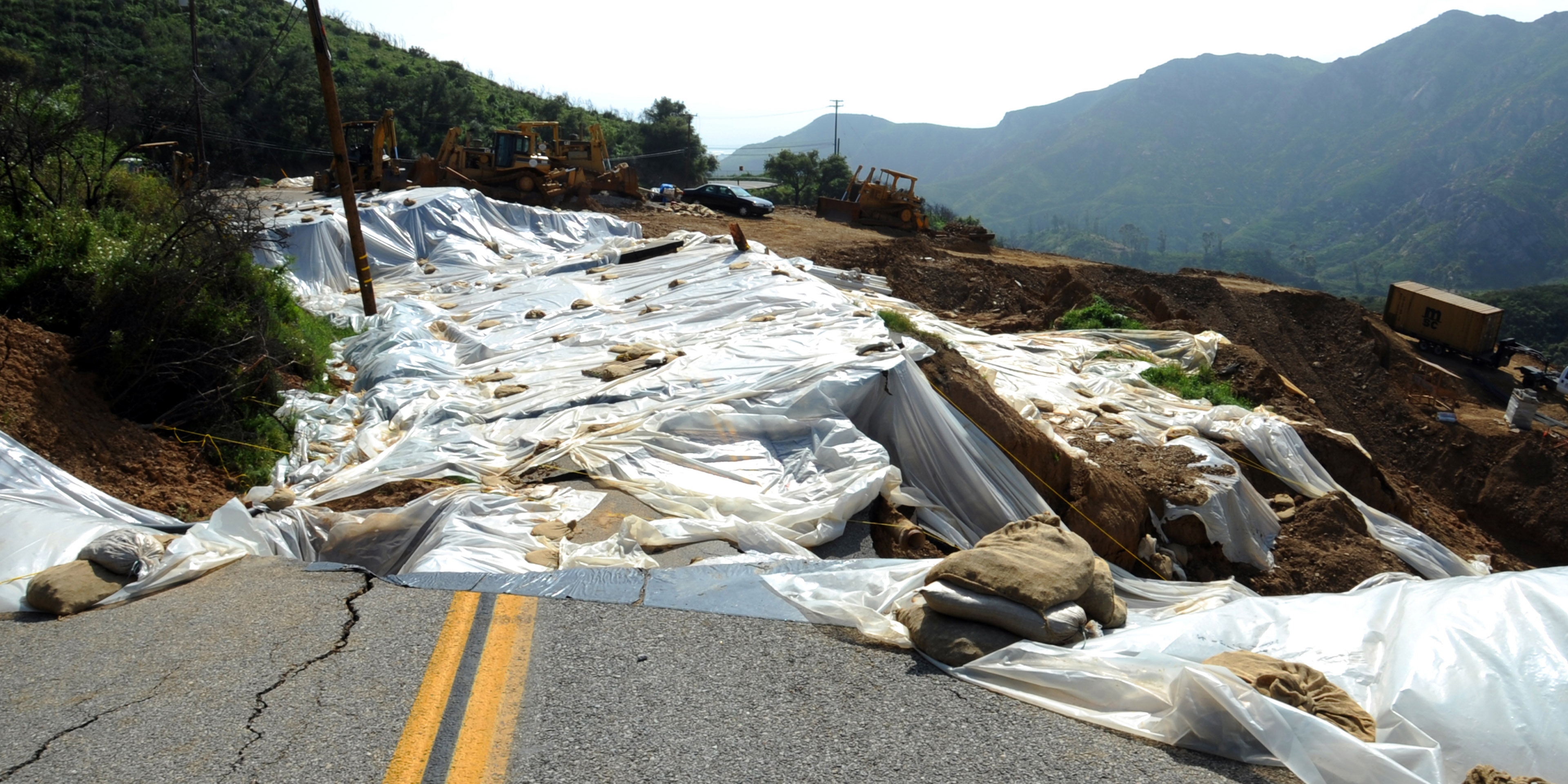 Hillside with a covering and various bulldozers and other heavy equipment after landslide on the hillside.