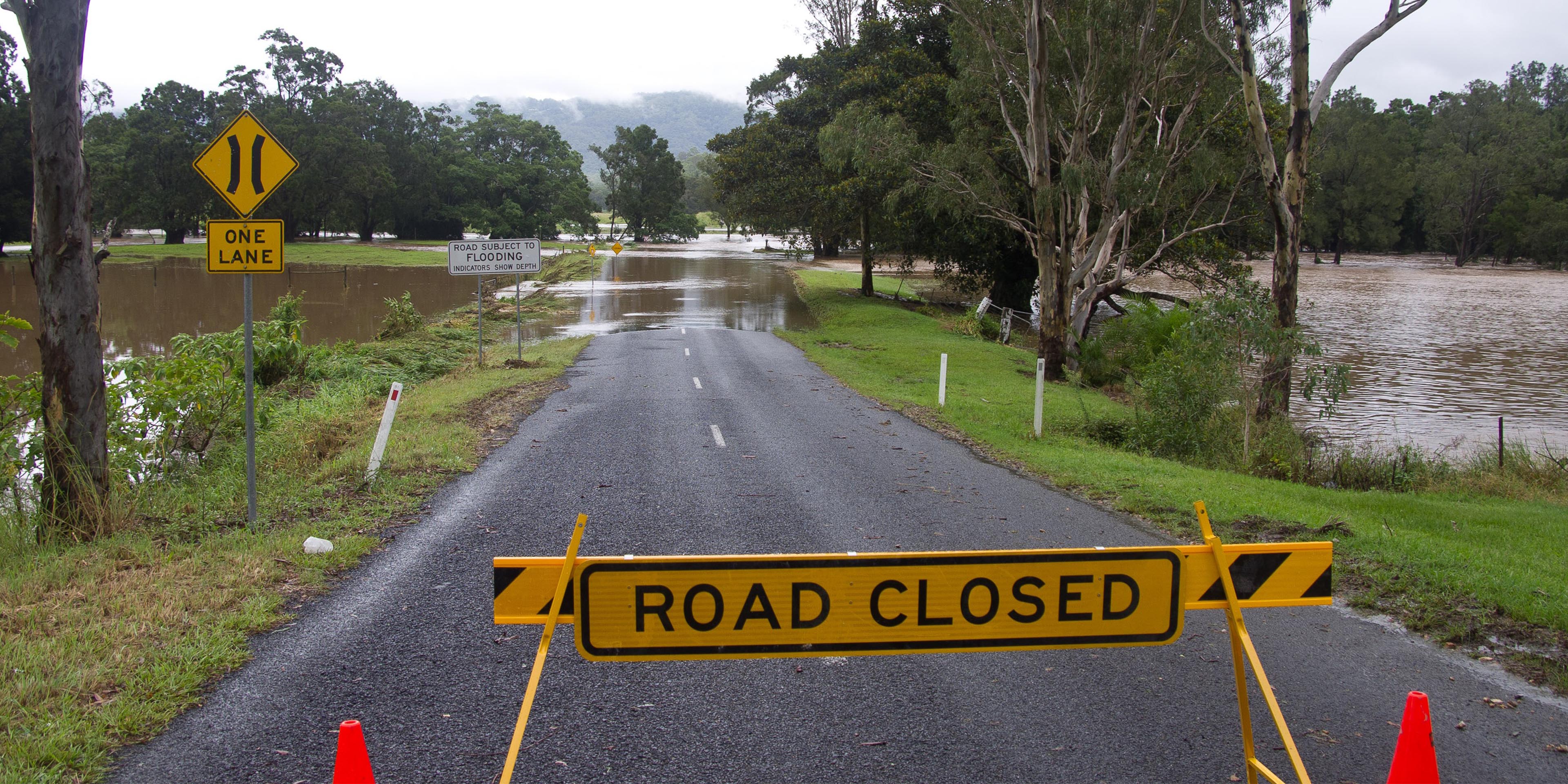 Road closed sign in front of flooded road with swollen river on both sides of the road.
